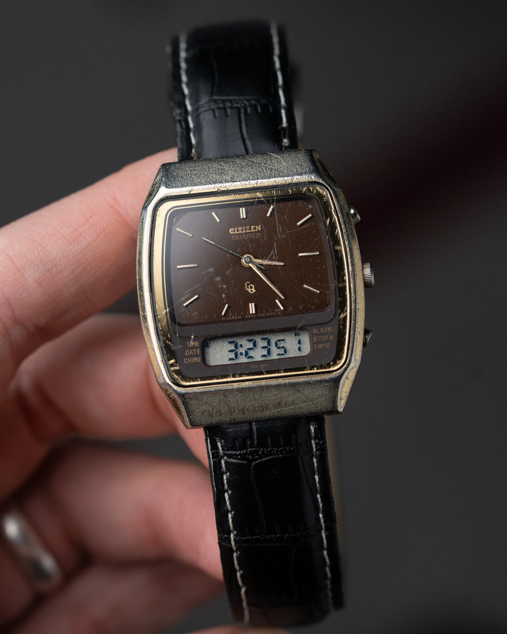 Vintage watch with black leather strap held by a hand against a dark background