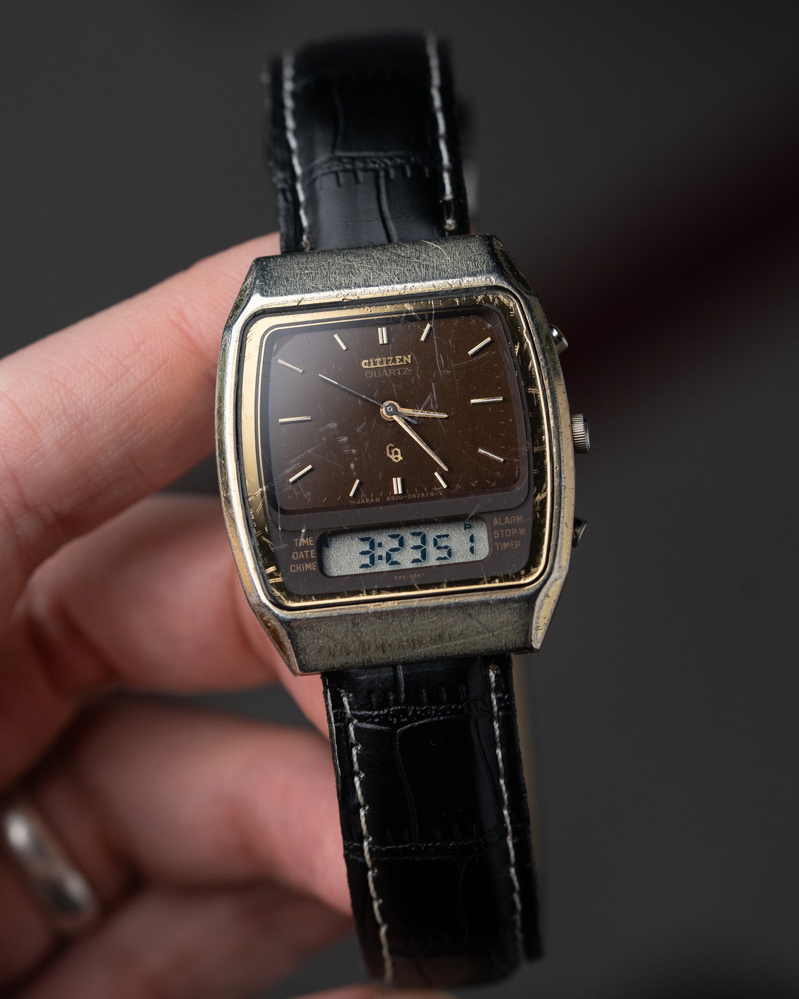 Vintage watch with black leather strap held by a hand against a dark background