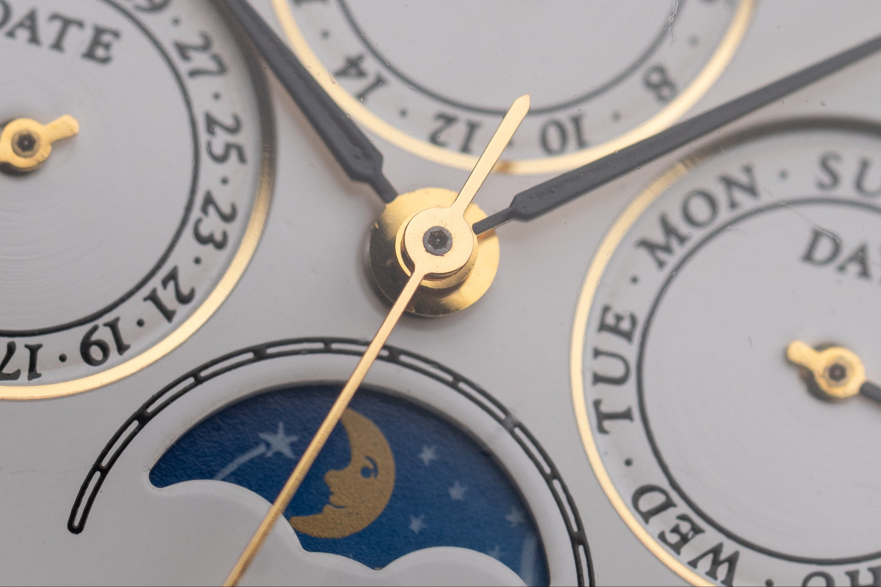 Close-up of a watch face with gold and black hands and moon phase indicator.