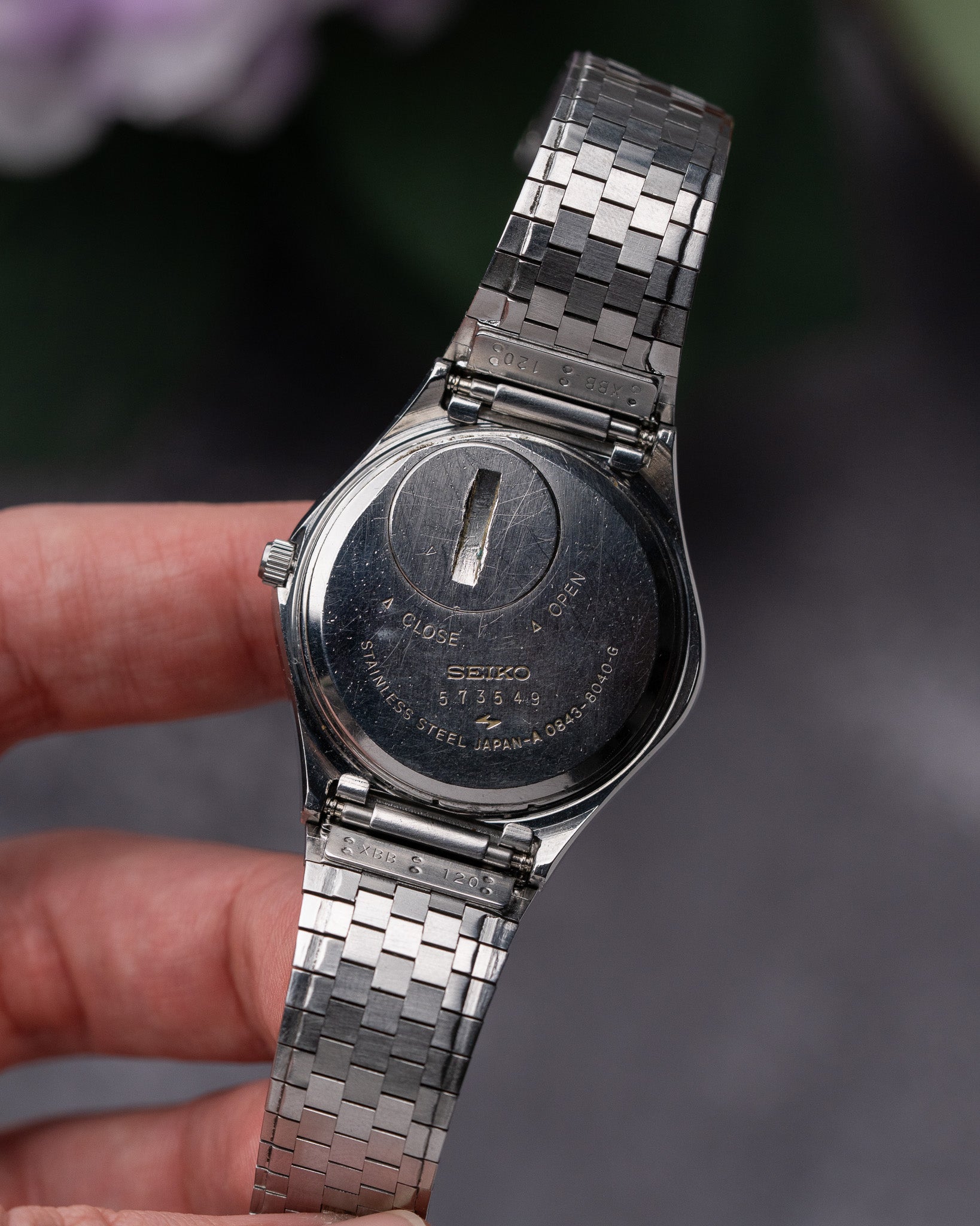 Silver Seiko watch being held by a hand with a blurred background