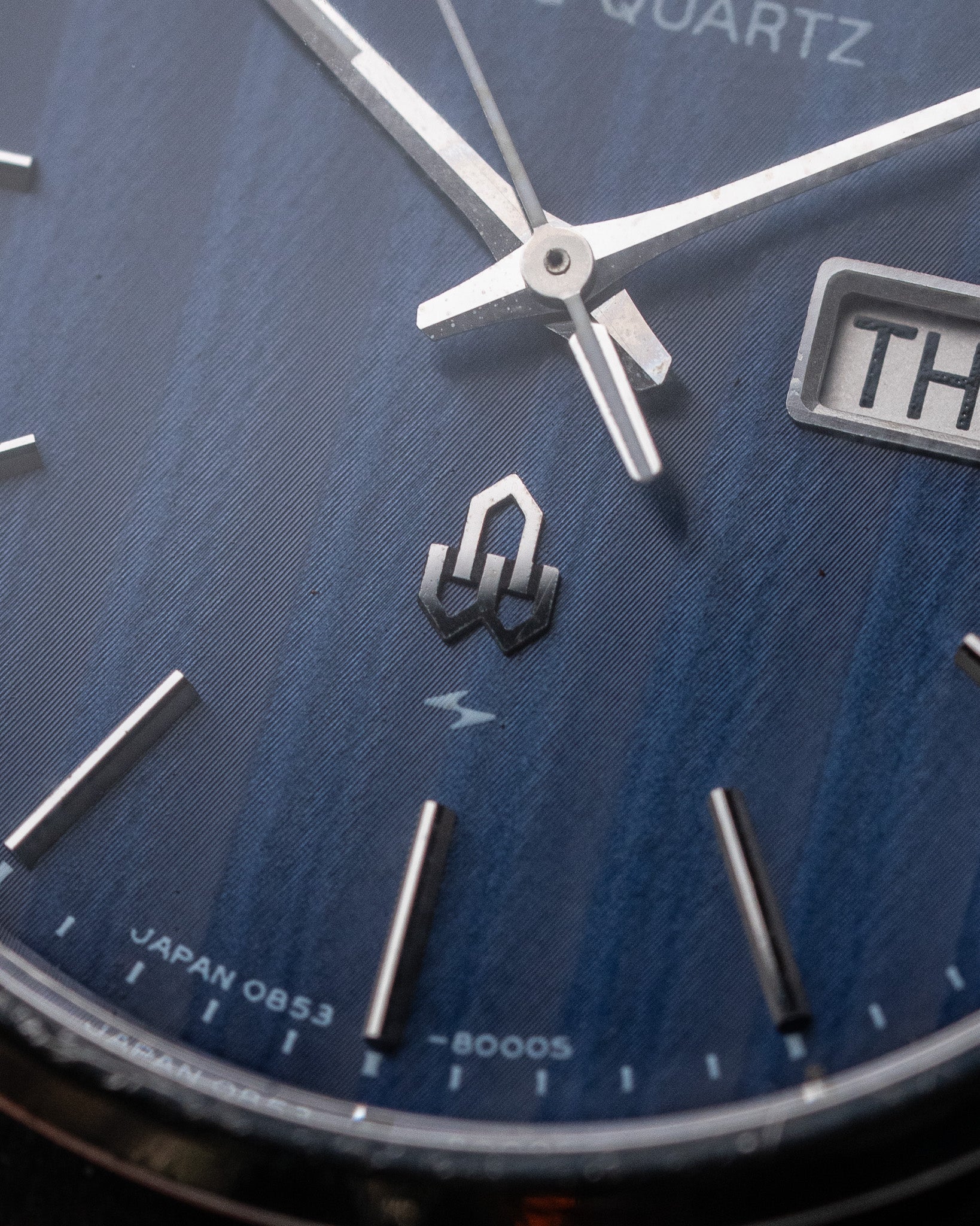 Close-up of a watch face with blue textured dial and silver accents.