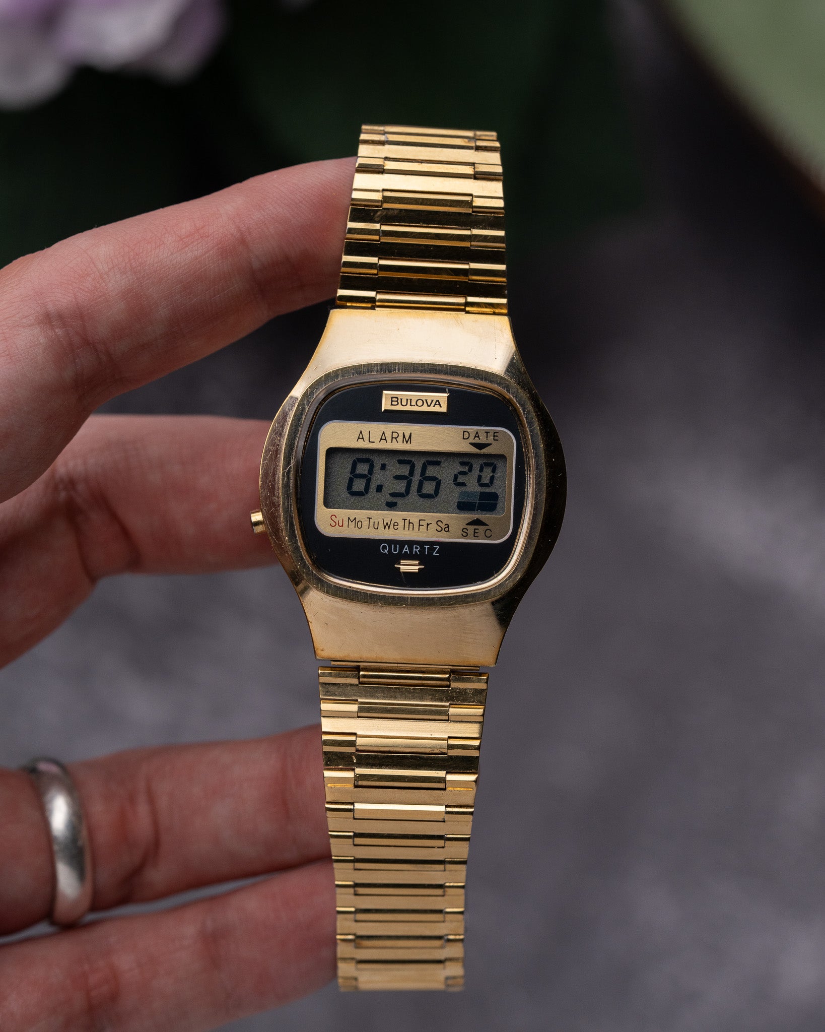 Gold digital watch held by a hand with a blurred background
