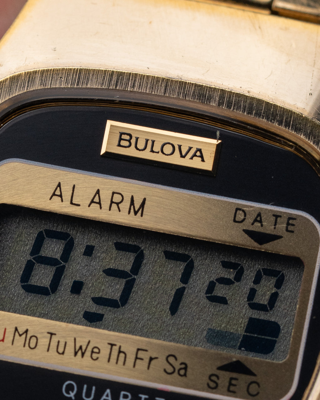 Close-up of a Bulova digital watch face with alarm and date display.