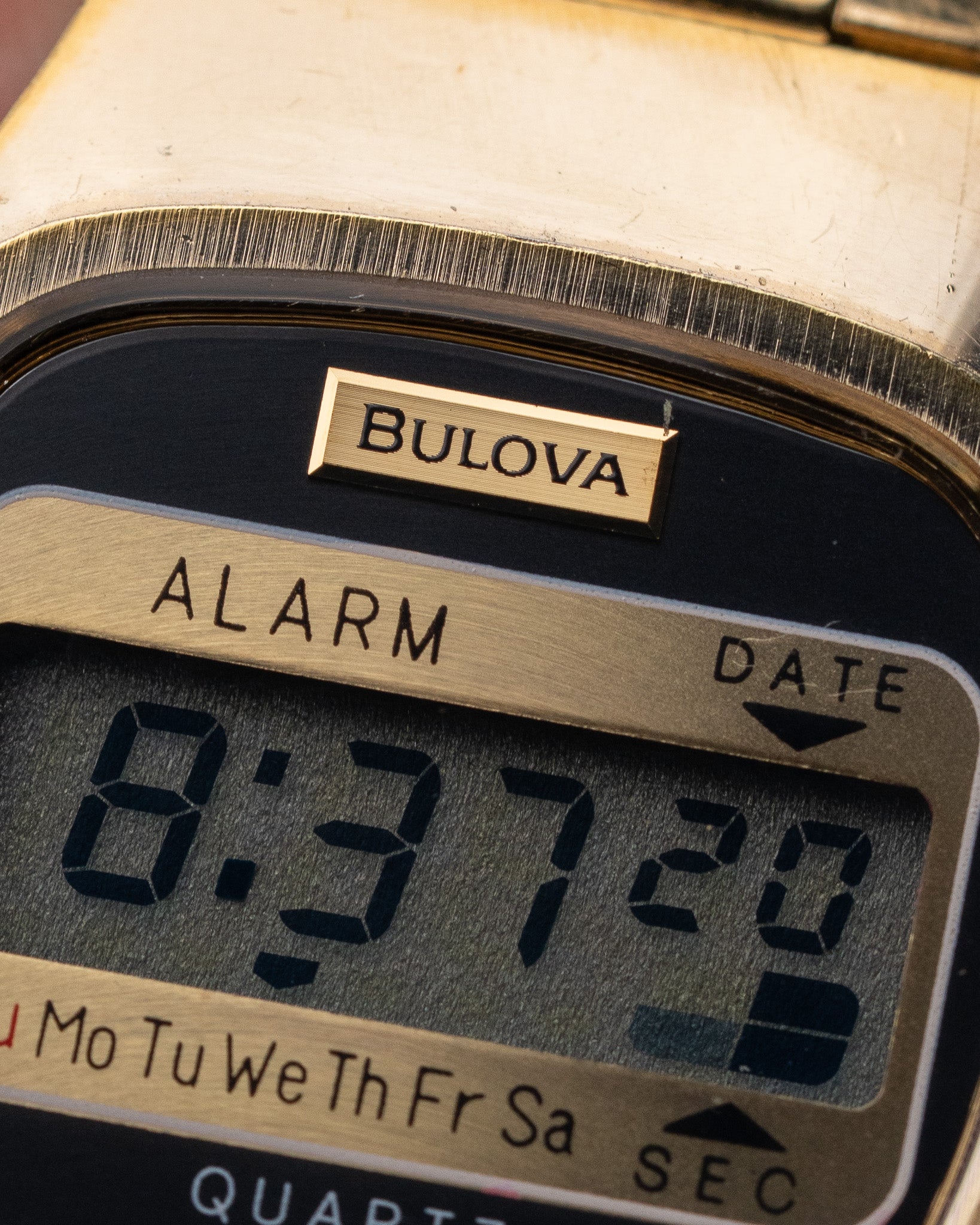 Close-up of a Bulova digital watch face with alarm and date display.